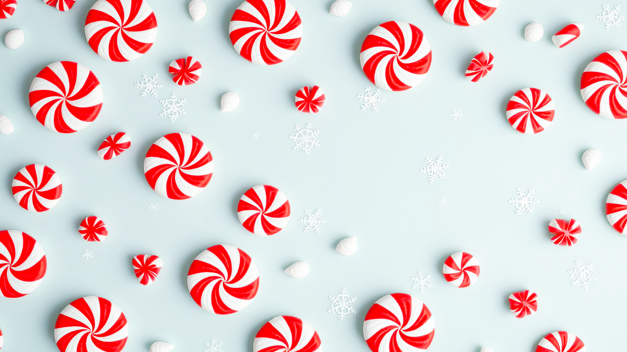 Festive holiday cocktail featuring London Liqueurs Santa Baby Candy Cane peppermint liqueur, garnished with a candy cane, served in a clear martini glass with crushed peppermint rim and shimmering holiday decor in the background